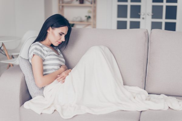 Woman Sitting on a Sofa with Blanket in Pain from Menstrual Cramps